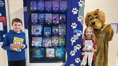 Fifth grade student Jaxon Cates and fourth grade student Mabrie Murphy, with Cedar Springs Elementary mascot Springer the Lion, were the first two randomly chosen students to pick a book from the school’s new book vending machine on Nov. 10. 
