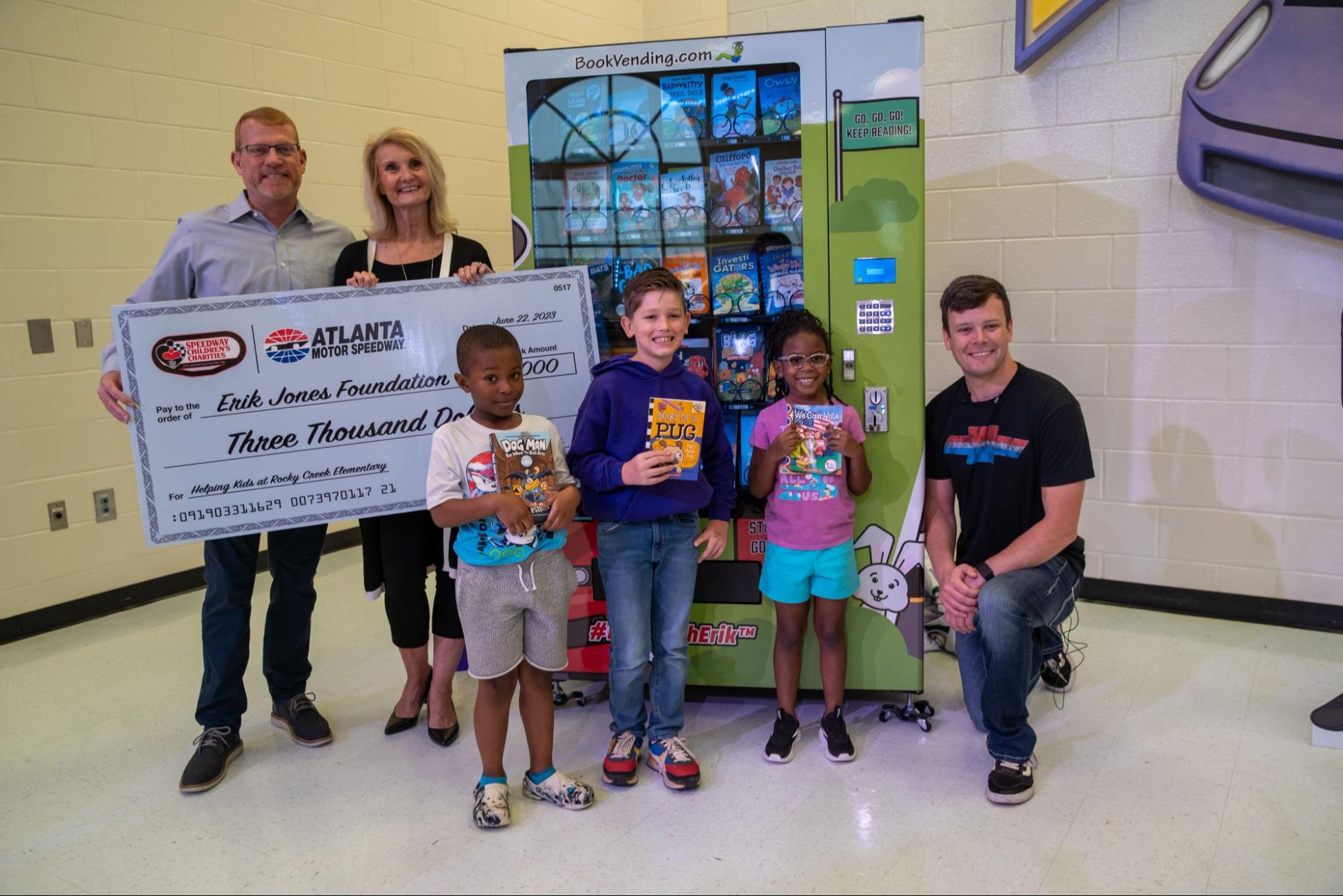 Erik Jones of NASCAR with administrators & students posing in front of Rocky Creek Elementary’s new Inchy bookworm book vending machine, proudly donated by Erik Jones Foundation.